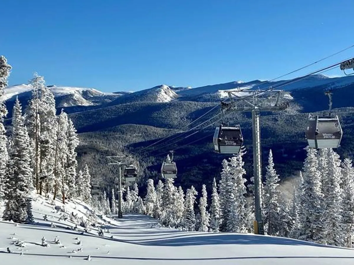 A scenic exterior view shows a ski lift gliding above a snow-covered mountain landscape, framed by tall evergreen trees. The scene evokes a sense of adventure and easy mountain access, with pristine slopes ready for winter activities.