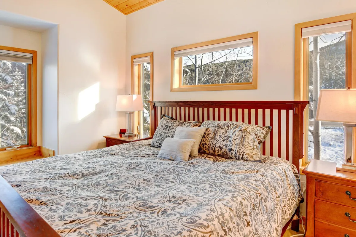 A tranquil bedroom featuring a bed with patterned bedding, a wooden bed frame, matching nightstands with soft lamps, and windows allowing natural light to pour in. The peaceful setup exudes comfort and calm, ideal for restful nights and rejuvenating mornings.