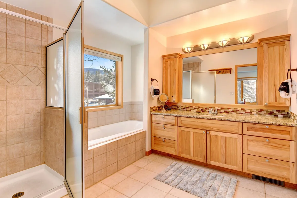 A spa-inspired bathroom with a large window offering natural views, elegant wooden cabinetry, and modern lighting fixtures. The space feels calming and luxurious, perfect for unwinding after a full day.