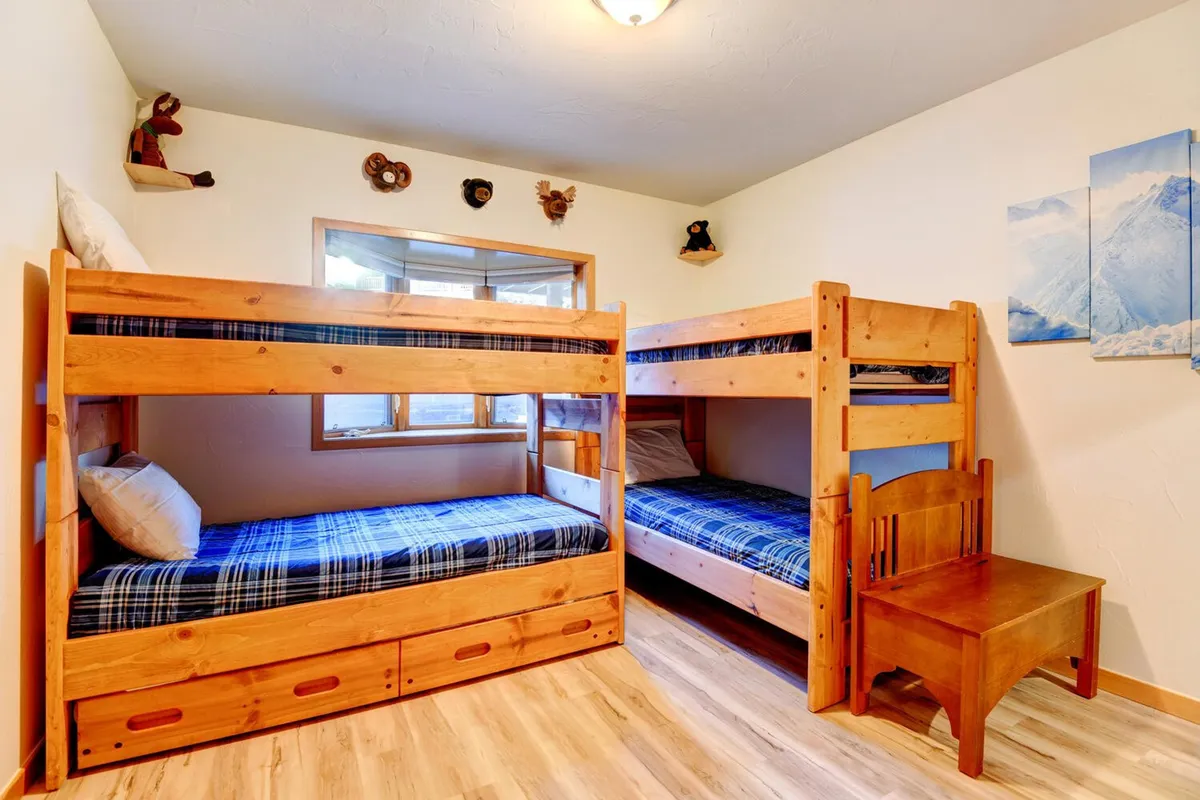 A playful bunk room with sturdy wooden bunk beds, cheerful wall art, and space for playing or storytelling. Sunlight lights up the room, creating an inviting environment for kids to play and enjoy sleepovers.