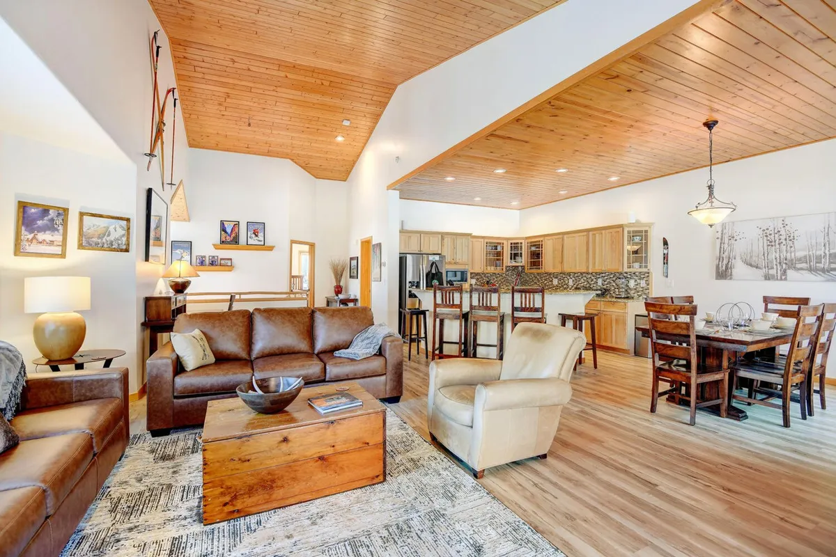 An open-plan living area with leather sofas, a wooden coffee table, a dining area, and a kitchen bar. The room is set up for socializing, game nights, dining, and storytelling, with a warm and inviting atmosphere that fosters togetherness.