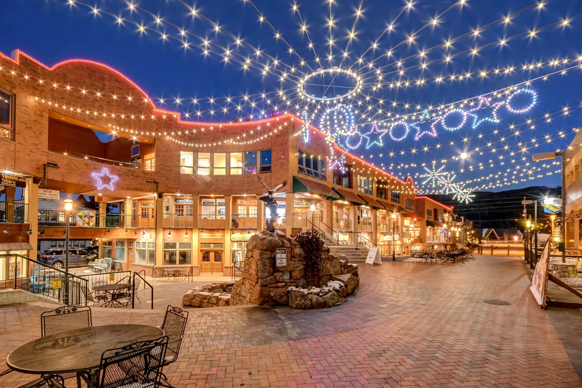 An inviting outdoor scene featuring string lights overhead, decorative star motifs, a stone fountain, and a comfortable outdoor seating area. The atmosphere is cheerful and lively, ideal for gatherings or simply enjoying the local ambiance.