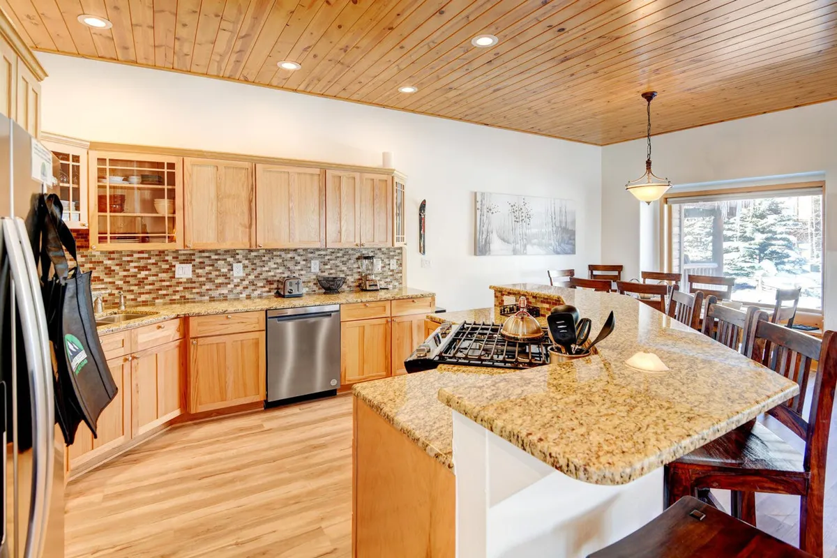 A welcoming kitchen scene with a granite countertop, wooden cabinetry, stainless steel appliances, and a dining area in view. Decorative wall art adds a touch of personality, and the space is clearly designed for meal preparation, gathering, and entertaining.