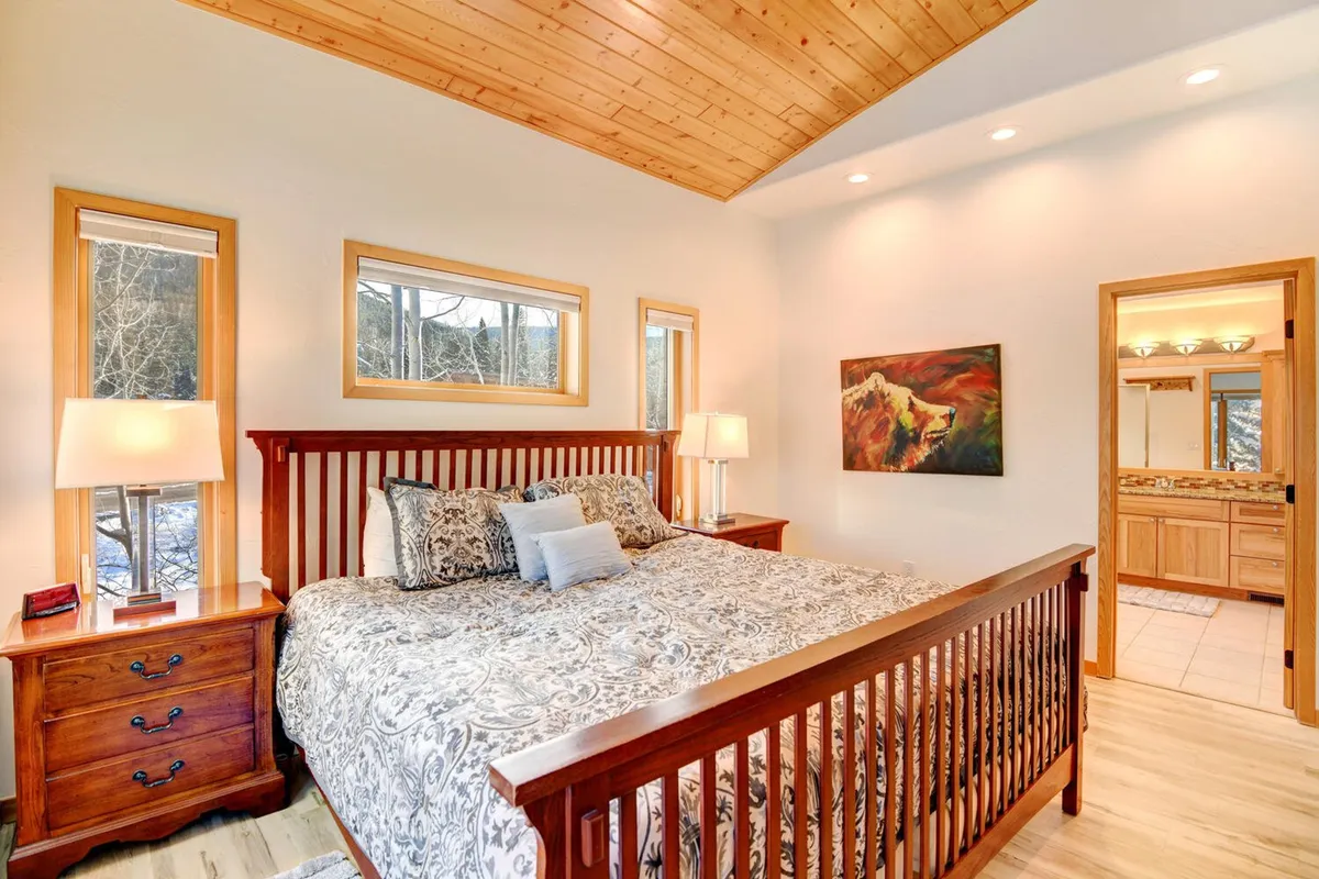 A restful bedroom with decorative bedding, wooden nightstands topped with cozy lamps, and framed artwork on the wall. Sunlight streams in, creating a peaceful ambiance perfect for relaxation or reading after a long day.