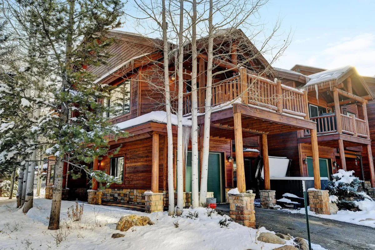 The image showcases the exterior of a luxurious single-family chalet nestled among aspen trees, featuring a snow-covered roof, a beautiful wooden balcony, and a solid stone foundation. Fresh snow blankets the yard, and the inviting balcony offers views perfect for watching snowfall or sipping cocoa. The scene radiates a cozy, welcoming winter atmosphere, hinting at family gatherings, outdoor fun, and relaxation.