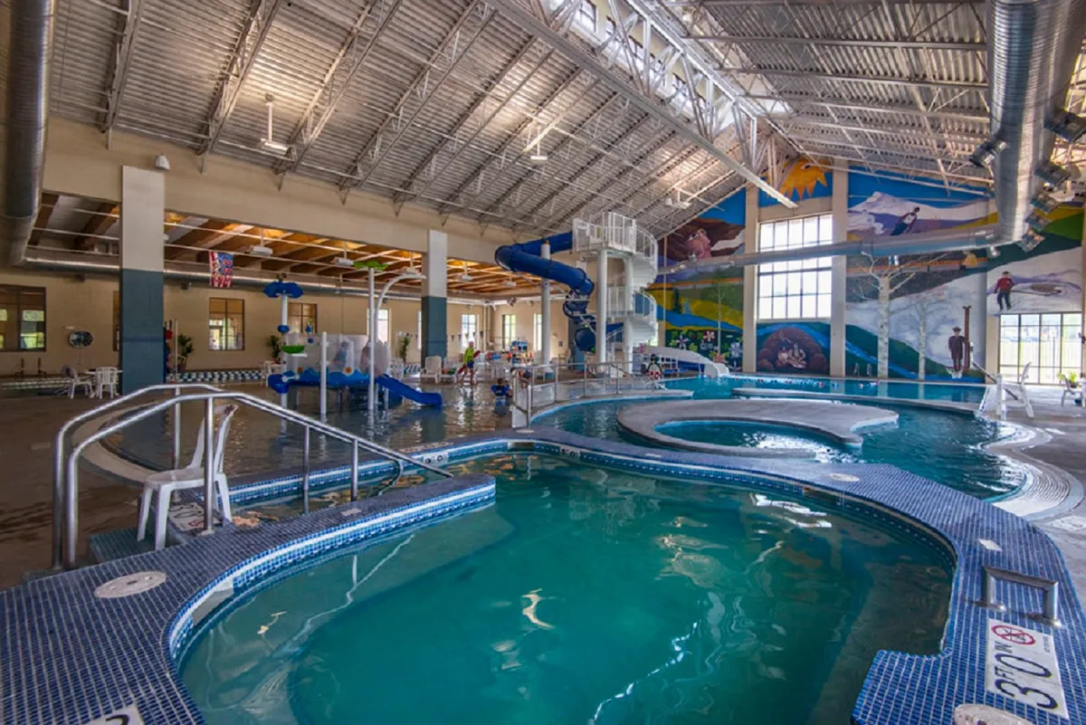A vibrant indoor recreation center scene featuring colorful water slides, multiple pool areas, a playful mural, and children gleefully playing. Families lounge on chairs while kids splash and laugh, capturing the essence of joyful group activity and all-ages fun.
