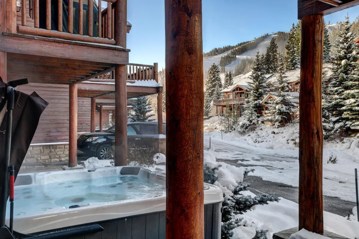 An inviting outdoor hot tub set against a backdrop of snow-covered landscape, with wooden pillars framing the space. The area exudes warmth and comfort, suggesting a relaxing soak while surrounded by winter scenery. The scene blends luxury with nature, hinting at cozy family moments after a day of adventure.