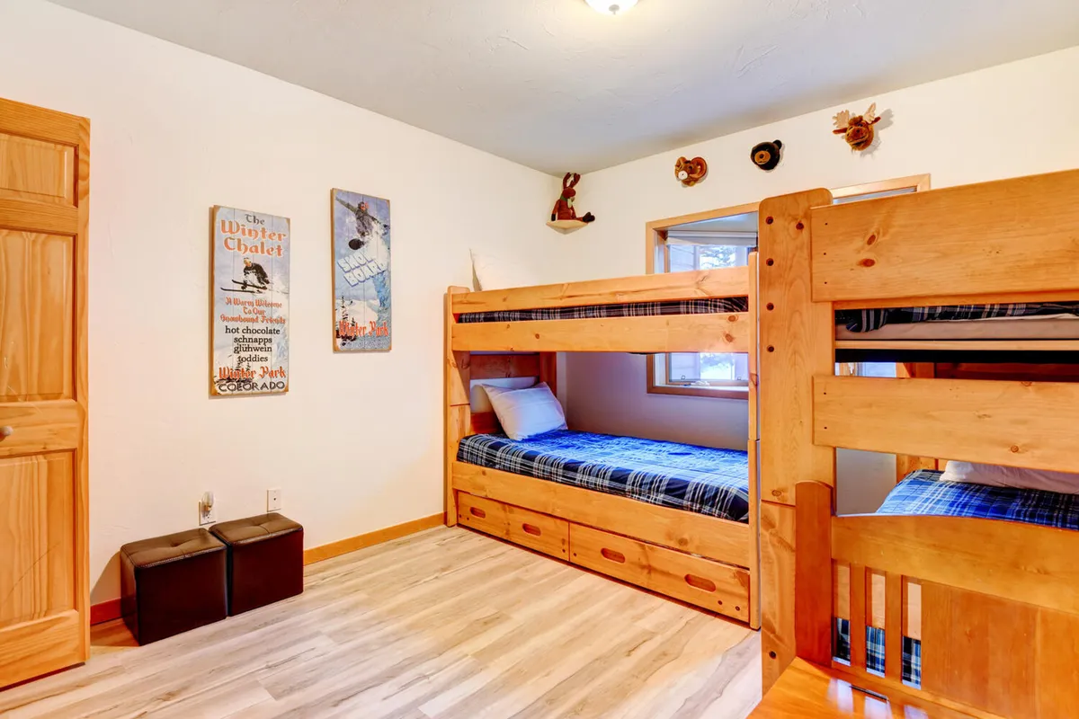 A playful and cozy bunk bed room with wooden furnishings, decorative wall art, and inviting bedding. The space is clearly designed for children, encouraging play, sleepovers, and games.